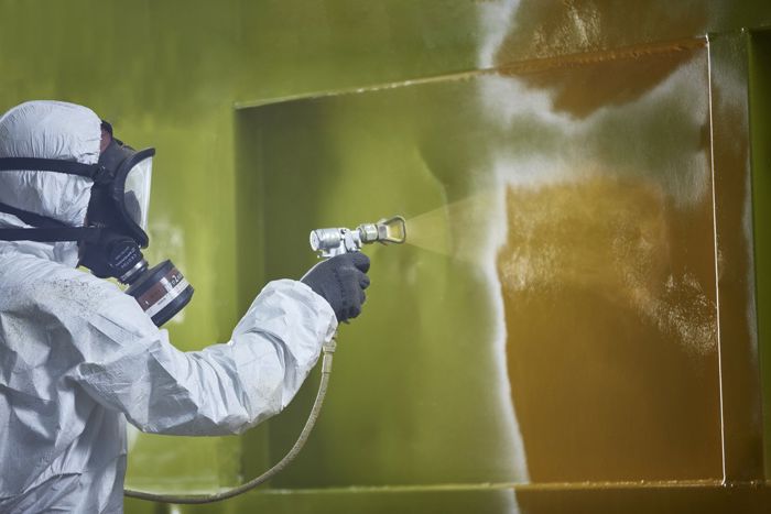 Ein person i verneutstyr sprøytelakkerer ein vegg